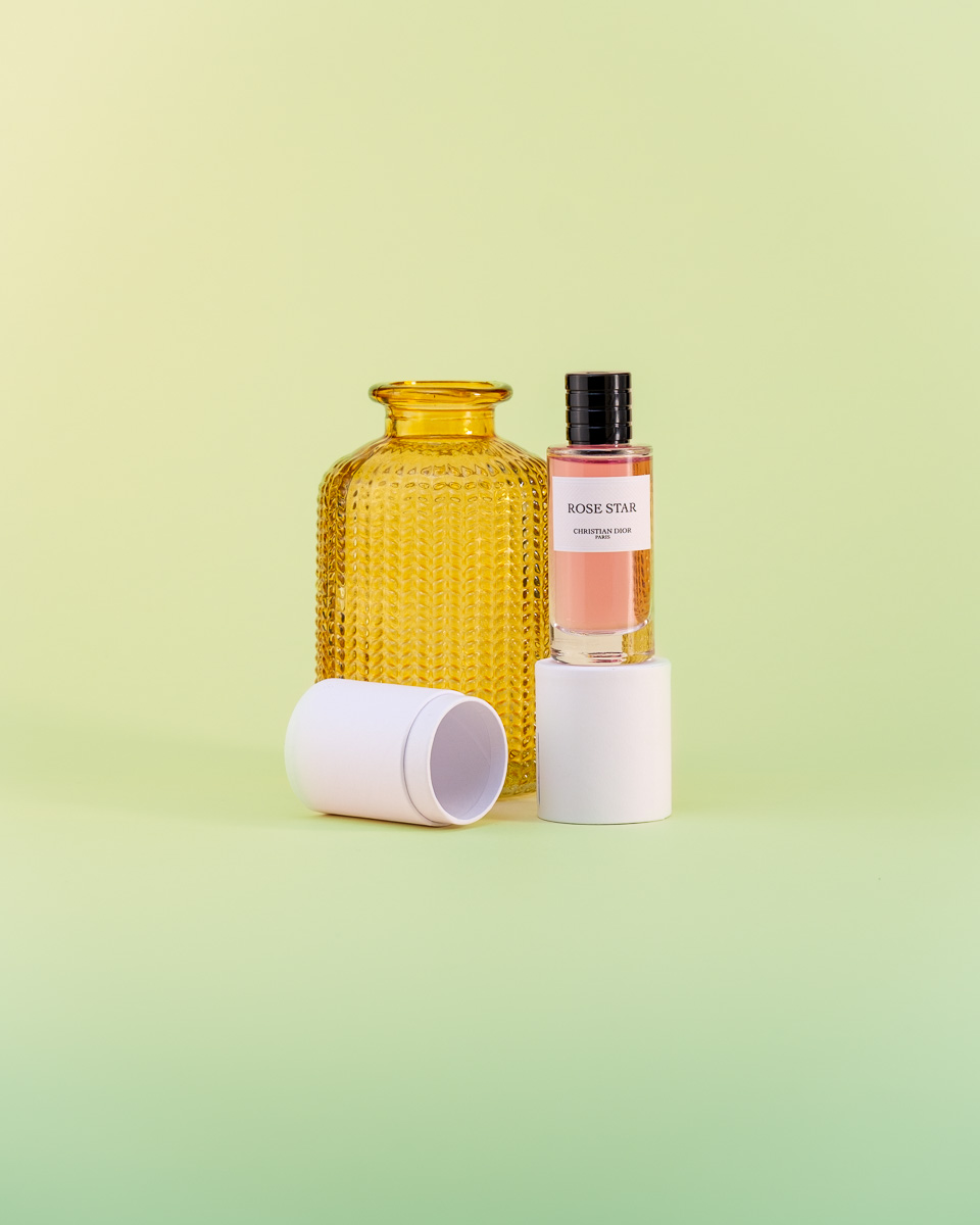 Photo produit d'un flacon de parfum ruse sur fond vert, lumière douce avec un petit flacon jaune en arrière plan