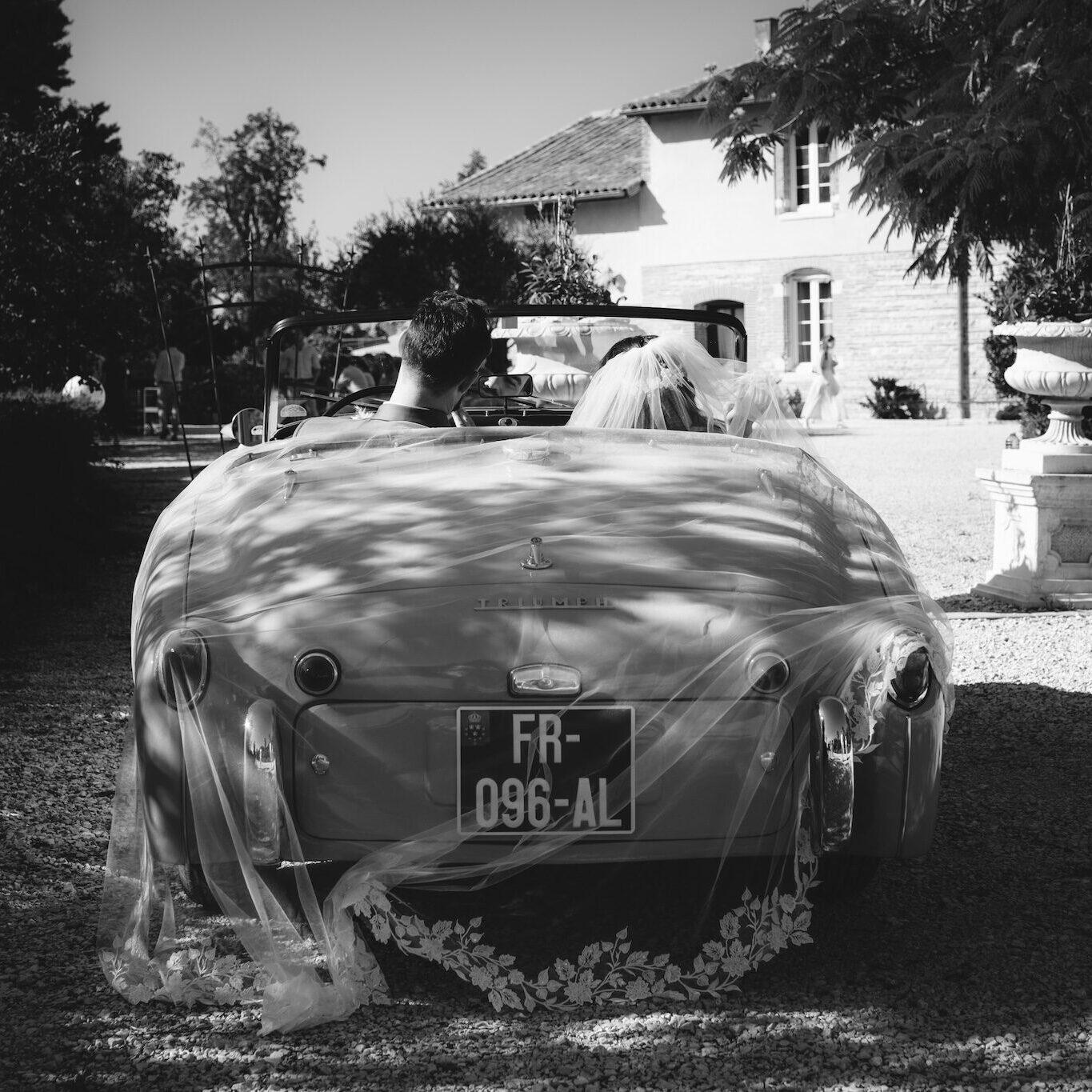 Mariés de dos dans une voiture décapotable devant le domaine du mariage