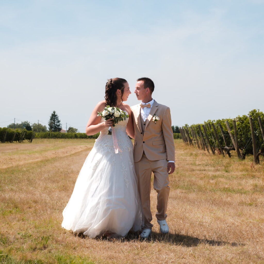 Mariés se tenant la main au milieu d'un champ de vigne, domaine de mariage en arrière plan